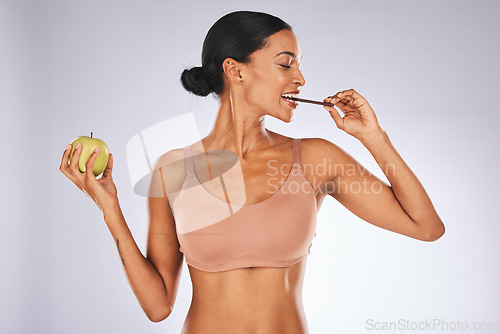 Image of Health, apple and diet of a healthy woman in studio with a fruit and chocolate for balance and motivation. Person on a grey background for nutrition, eating and to lose weight with nutrition benefits