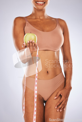 Image of Black woman, apple and measure tape for diet, wellness and healthy lifestyle with lady on grey studio background. African American female, girl and fruit for health, size and fitness for confidence
