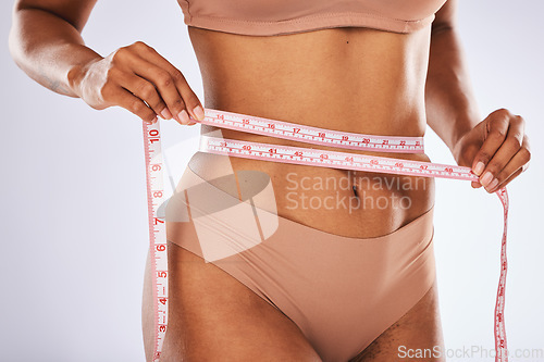 Image of Measuring tape, stomach and woman in studio for wellness, weight loss and tummy tuck on grey background. Belly, measurement and girl model checking for progress, slimming and size after detox or diet