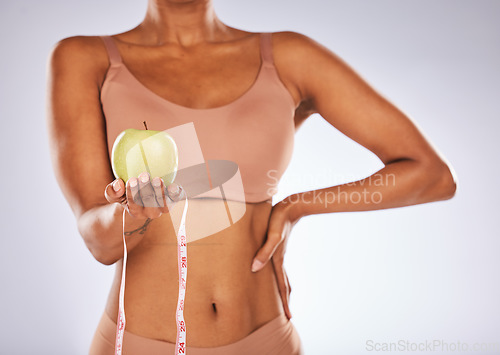 Image of Apple, measuring tape and diet with a black woman in studio on a gray background for weightloss. Food, fitness and health with a female posing to promote exercise, nutrition or health eating