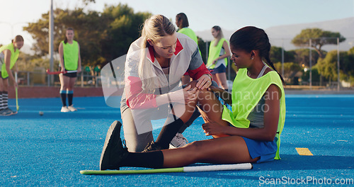 Image of Woman, sports and knee injury in hockey training, practice or game on a blue turf with coach and team. Sport mentor helping female in leg pain, accident or bruise from physical activity during match