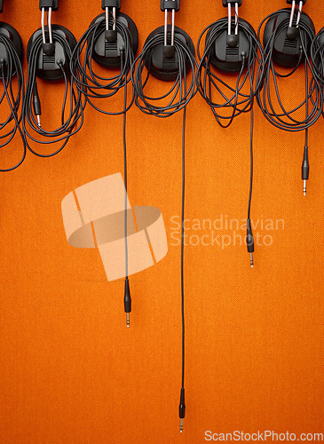 Image of Audio, cables and mockup on an orange wall background in a music studio for recording or sound engineering. Media, equipment and hanging wires in an empty room of a record label for production