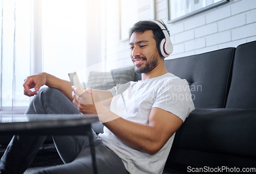 Image of Phone, music and man with headphones in home living room streaming radio or podcast. Cellphone, technology and male in lounge sitting on floor listening to song, audio or album on mobile smartphone.