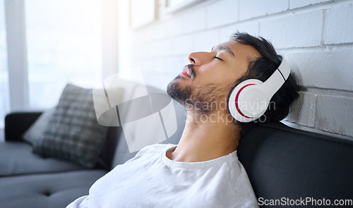 Image of Relax, music and man with headphones on sofa in home living room streaming radio or podcast. Meditation, technology and male on couch in lounge listening to peaceful song, audio or album in house.