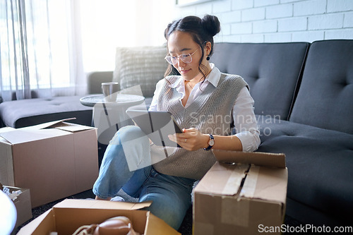 Image of Real estate, tablet and Asian woman moving into new home while planning or calculating mortgage online. Relocation boxes, technology and female property owner or remote worker in living room of house