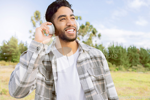 Image of Music, smile and man with headphones in forest, happy and relax on blue sky, tree and space background. Radio, earphones and guy, smile and joy while listening to audio, podcast or track in forest