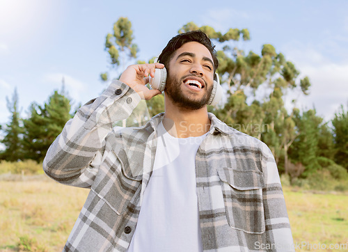 Image of Music, happy and man relax in a park, smile and laughing at podcast or audio track against nature background. Earphones, laugh and handsome guy listening to online comedy, song or playlist in forest