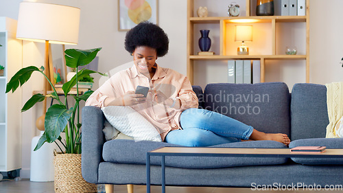 Image of Laughing woman listening to music and sending a message with funny memes on her phone and drinking coffee while on the sofa. Happy black female browsing social media and surfing the internet online