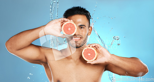 Image of Man, portrait smile and fruit for skincare, healthy nutrition or vitamin C and hydration against a blue studio background. Happy male holding grapefruit for natural organic diet or body wellness