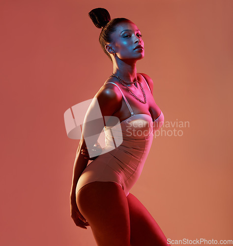 Image of Portrait, beauty and neon with a model black woman in studio posing in underwear on an orange background. Aesthetic, art and fashion with an attractive young female standing on a kaleidoscope wall