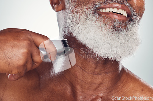 Image of Hand, beard and shaving with an electric razor with a mature black man in studio on a gray background. Face, grooming and hygiene with a mature male in the bathroom to shave for hair removal