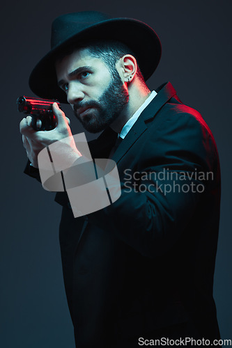 Image of Gangster, suit and shooting gun on dark studio background in secret spy, isolated mafia leadership and crime lord security. Model, man and hitman aiming weapon in formal or fashion clothes aesthetic