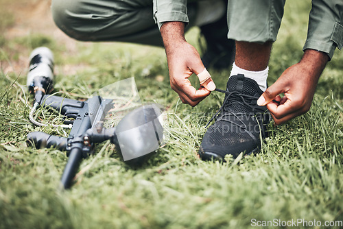 Image of Paintball, gun and shooter or man kneeling ready for competitive match or competition in the forest. Player, athlete and person tying laces with game equipment or weapon on a sports field