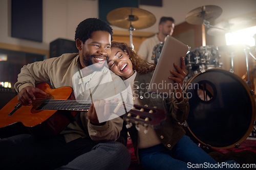 Image of Musician, guitar and couple with a tablet for music, email and learning sound in a dark studio. Happy, reading and black man and woman streaming on technology with a musical instrument at night