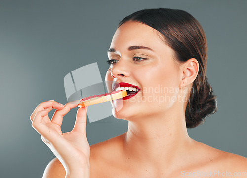 Image of Fruit, smile and woman with a grapefruit for nature and wellness aesthetic in a studio. Model health eating, beauty and natural skincare of person with red lipstick hungry for vitamin c nutrition