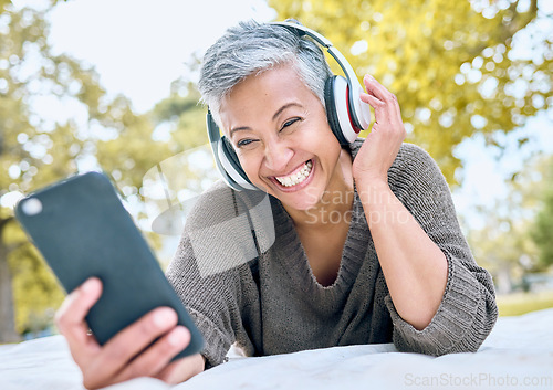 Image of Headphones, music and old woman with phone at park streaming radio or podcast. Social media, cellphone and happy, elderly and retired female with mobile, laughing at funny meme and enjoying audio.