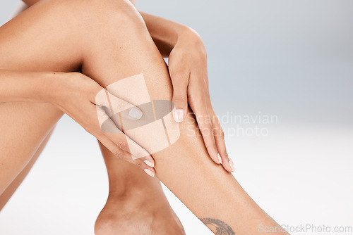 Image of Legs, skin care and body of a woman in studio for hair removal, epilation or waxing for smooth shine. Natural model person hands for spa beauty treatment, health and wellness on a grey background