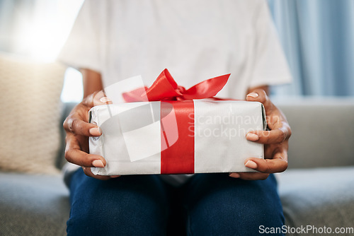 Image of Box, gift and woman on a sofa in the living room with a giving gesture for celebration or event. Bow, wrapping paper and African female with a present for christmas, birthday or holidays in a house.