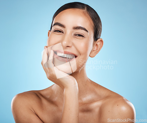 Image of Portrait, beauty and smile with a model woman in studio on a blue background for natural skincare. Face, skin and cosmetics with an attractive young female posing to promote a luxury product