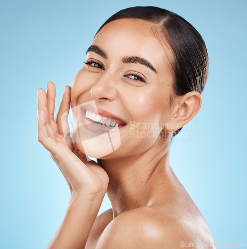 Image of Portrait, hand and smile with a model woman in studio on a blue background for beauty or skincare. Face, skin and cosmetics with an attractive young female posing to promote a luxury product