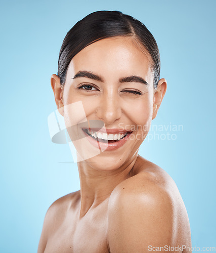 Image of Portrait, wink and skincare with a model woman in studio on a blue background for natural beauty. Face, skin and winking with an attractive young female posing to promote a luxury cosmetic product