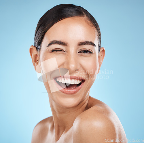 Image of Face, wink and beauty skincare of woman in studio isolated on blue background. Portrait, makeup and cosmetics of happy female model with healthy, glowing and flawless skin after spa facial treatment.