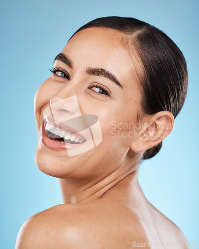 Image of Portrait, smile and happy with a model woman in studio on a blue background for beauty or skincare. Face, skin and cosmetics with an attractive young female posing to promote a luxury product