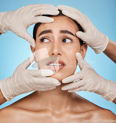 Image of Hands, woman face and plastic surgery, skincare or treatment against a blue studio background. Hand and gloves touching female in medical botox, aesthetic change or liposuction for facial implants