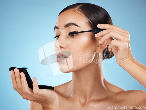 Image of Mascara, application and woman with makeup and mirror isolated on a blue background in a studio. Skincare, beauty and model with cosmetics for an event, party or fancy celebration on a backdrop