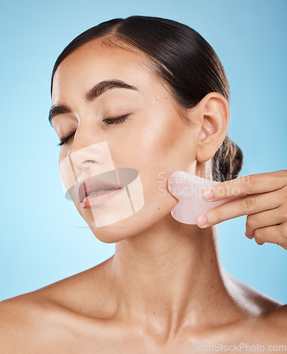 Image of Face massage, gua sha and skin care woman for dermatology, cosmetics and wellness. Young aesthetic model person for natural stone spa product for facial glow, lines and to relax on blue background