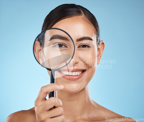 Image of Magnifying glass, face portrait and skincare of woman in studio isolated on a blue background. Beauty search, makeup and cosmetics of female model with magnifier lens to check aesthetic wellness.