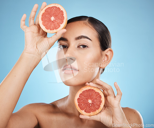 Image of Face, portrait and skincare of woman with grapefruit in studio isolated on a blue background. Organic cosmetics, food and female model with fruits for nutrition, healthy diet or vitamin c for beauty.