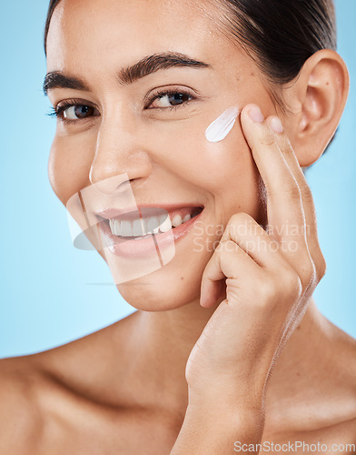 Image of Portrait, cream and skincare with a model woman in studio on a blue background for natural skincare. Face, skin and lotion with an attractive young female posing to promote a luxury cosmetic product