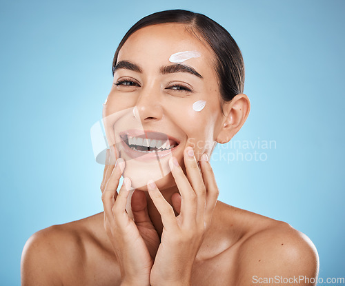 Image of Portrait, hands and cream with a woman in studio to apply treatment on a blue background for beauty. Face, skincare and lotion with an attractive young female posing to promote a luxury product