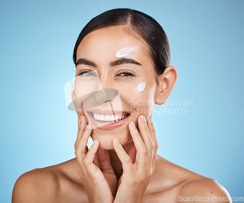 Image of Face cream, skincare portrait and woman in studio isolated on a blue background. Cosmetics, dermatology and happy female model apply lotion, creme or moisturizer for beauty, aesthetics and wellness.