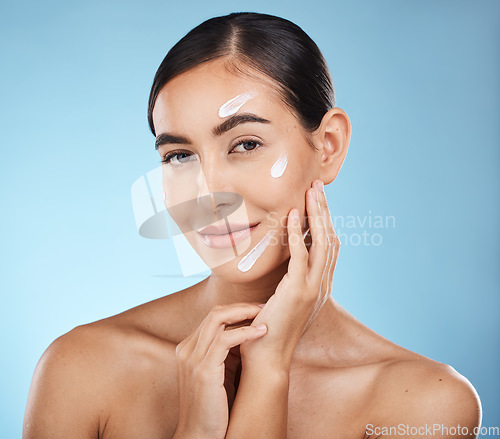 Image of Portrait, beauty and cream with a woman in studio to apply treatment on a blue background for skincare. Face, skin and lotion with an attractive young female posing to promote a luxury product