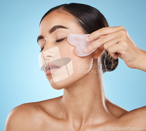 Image of Skin care, facial massage and beauty woman with gua sha for dermatology, cosmetics and wellness. Young model person with natural stone or spa face product to relax and glow on blue background