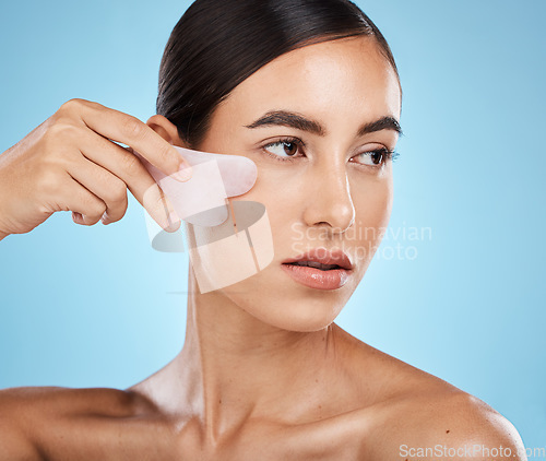 Image of Skin care, face massage and beauty woman with gua sha for dermatology, cosmetics and wellness. Aesthetic model person with facial scraping stone spa product to relax and glow on blue background