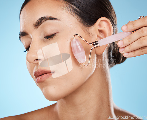 Image of Skin care, face roller and beauty woman with facial massage for dermatology, cosmetic and wellness. Young aesthetic model person for natural rose quartz spa product to relax on blue background