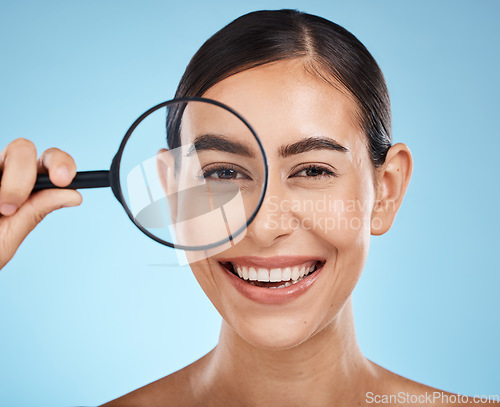 Image of Face portrait, magnifying glass and skincare of woman in studio isolated on a blue background. Beauty search, makeup and cosmetics of female model with magnifier lens to check aesthetic wellness.