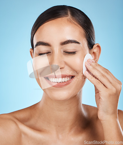 Image of Beauty, cotton pad and woman in a studio removing makeup, cosmetic or face glamour. Self care, skincare and happy female model with a healthy facial or skin routine isolated by a blue background.