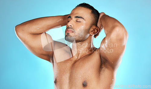 Image of Shower, hair and man in water splash for skincare, grooming and washing in studio on blue background. Cleaning, beauty and male model relax in luxury, treatment and haircare routine while isolated