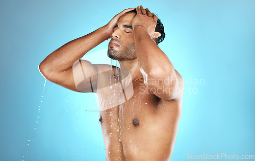 Image of Hair, shower and man in water splash for skincare, grooming and washing in studio on blue background. Cleaning, beauty and male model relax in luxury, treatment and haircare routine while isolated