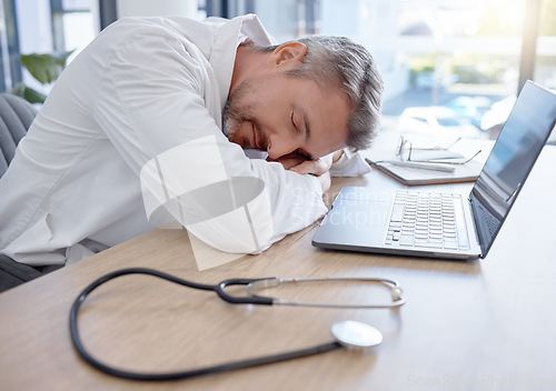 Image of Man, doctor and laptop sleeping on desk from burnout, overworked or insomnia at the office. Tired male medical professional taking a nap, rest or asleep on table by computer at the workplace