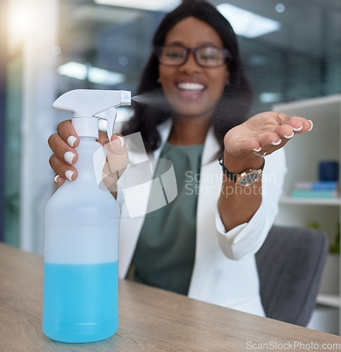 Image of Hand, covid and sanitizer with a business black woman in her office, sitting at a desk with her spray bottle. Health, safety and cleaning with a female employee using chemical disinfectant at work