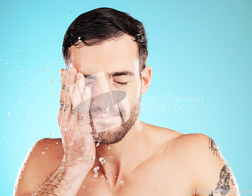 Image of Water drop, skincare and man with hand on face, morning cleaning treatment isolated on blue background. Facial hygiene, splash and male model grooming for health, wellness and spa skin care in studio