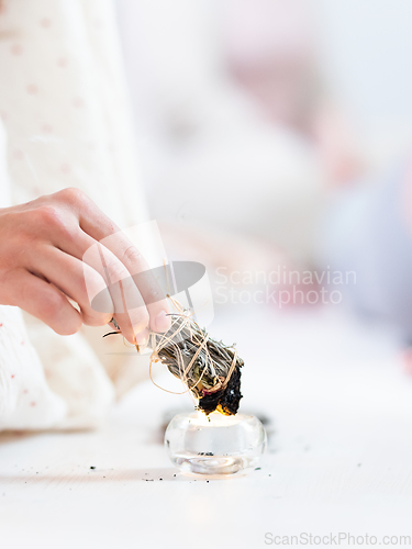 Image of Woman lighting a smudge kit with herbal stick. Natural elements for cleansing environment from negative energy, adding positive vibes. Spriritual wellness practices.