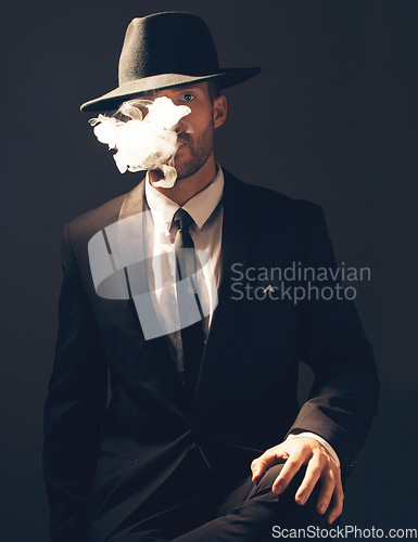 Image of Mafia, portrait and man with smoke in a suit for fashion isolated on a dark background in a studio. Sexy, vintage and businessman looking stylish, gangster and rich while smoking on a studio backdrop