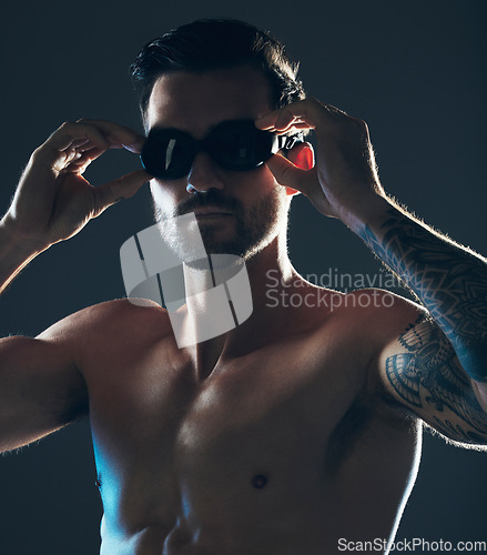 Image of Fitness, sports and face of swimmer with goggles isolated in studio for wellness, exercise and training. Workout, swimming athlete and man focus on dark background with muscle, strong body and tattoo