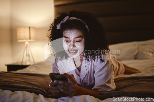 Image of Skincare, face mask and woman on a phone in her bedroom networking on social media or mobile app. Beauty, self care and female browsing the internet or typing a message while relaxing on her bed.